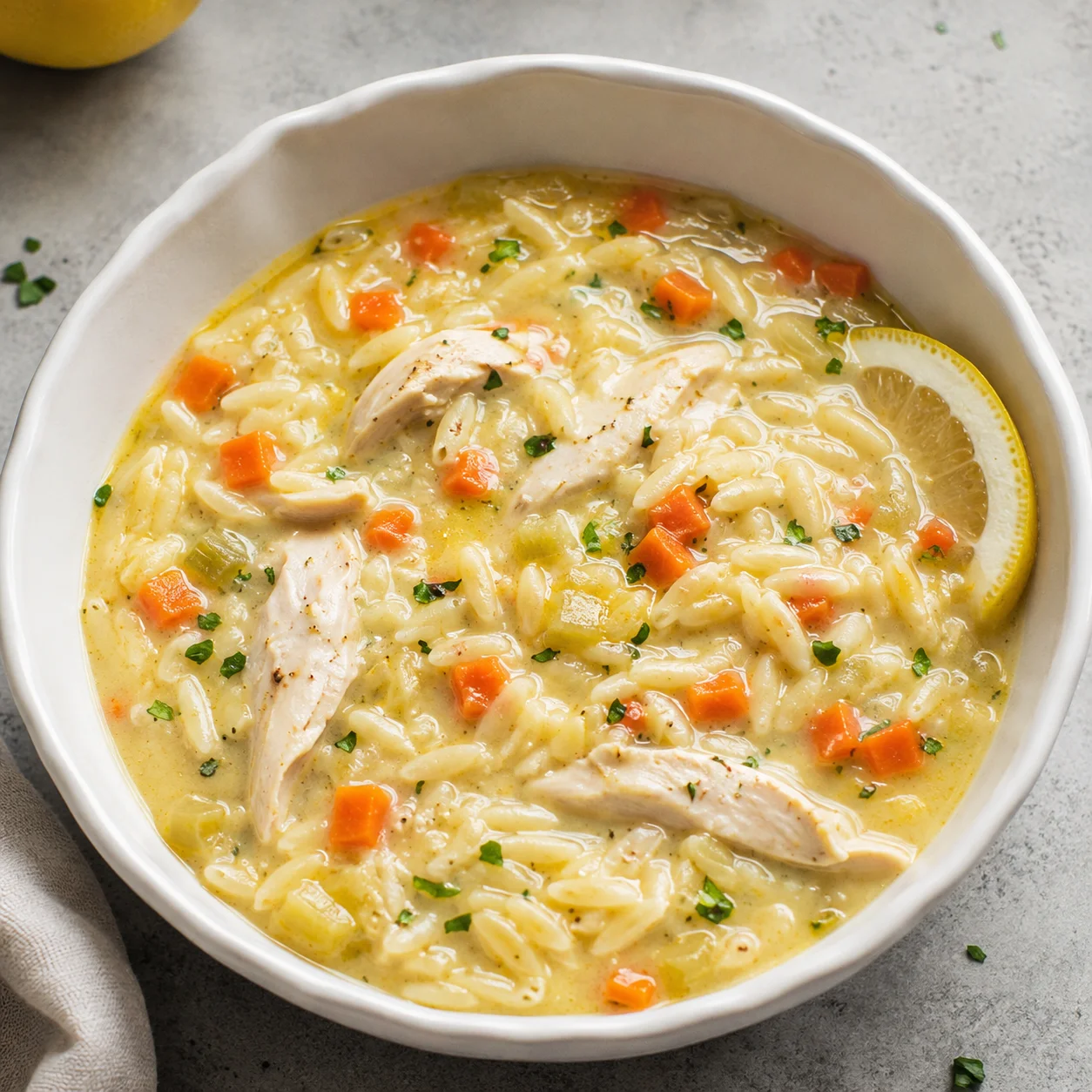 Lemon Chicken Orzo Soup with tender chicken, carrots, celery, orzo, parsley, and lemon in a white bowl
