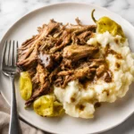Mississippi Pot Roast with tender shredded beef, mashed potatoes, and pepperoncini on a white plate