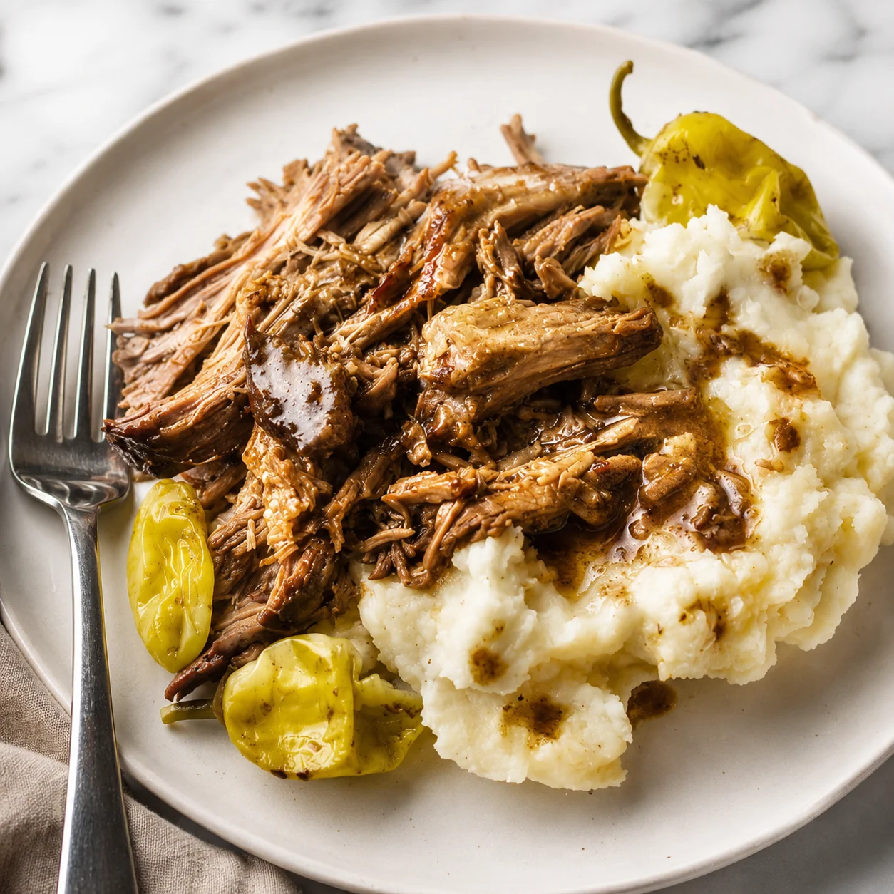 Mississippi Pot Roast with tender shredded beef, mashed potatoes, and pepperoncini on a white plate