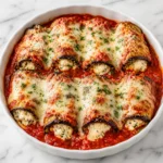 A fork lifts cheesy eggplant rollatini from marinara sauce, showing herb-speckled ricotta filling, stretchy melted cheese, and browned eggplant edges on white marble.