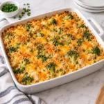 Chicken broccoli rice casserole baked in a white ceramic casserole dish on a bright white marble surface, with creamy rice, chicken pieces, broccoli florets, melted cheddar, and a lightly golden breadcrumb topping.