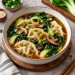 Potsticker soup with tender dumplings, sliced mushrooms, bok choy, scallions, and sesame seeds in a savory brown broth, served in a complete ceramic bowl on a bright marble surface.