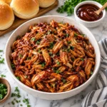 BBQ pulled chicken in a complete speckled cream bowl on a bright white marble surface, with glossy shredded chicken texture and an elegant food-blog presentation.