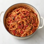 Spaghetti Fra Diavolo served in a complete cream-colored pot on a clean bright white marble surface, with realistic chunky tomato sauce and chili flakes, photographed without extra props or background clutter.