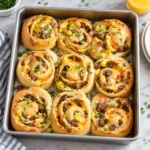 Golden breakfast rolls filled with egg, sausage, and melted cheese in a complete modern metal baking tray on bright white marble, with crisp browned edges and a soft, savory interior.
