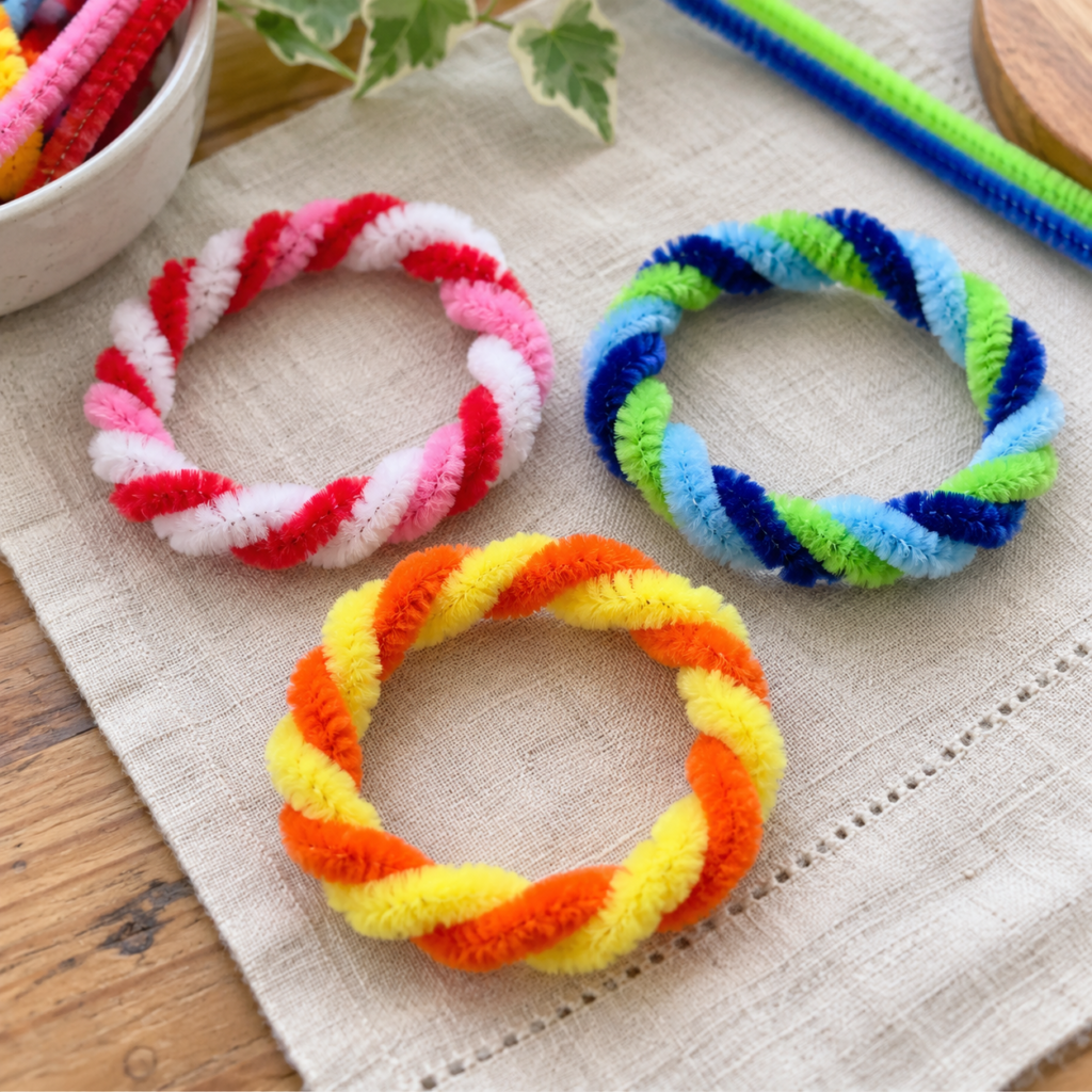 Colorful pipe cleaner crafts for kids, including handmade flowers, butterflies, friendship bracelets, caterpillars, pencil toppers, fish, and a heart garland.