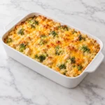 Cheesy broccoli chicken and rice casserole with golden cheddar in a white ceramic baking dish on white marble.