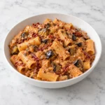 Rigatoni with eggplant and sun dried tomatoes in creamy ricotta sauce, served in a white ceramic bowl on white marble.