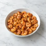 Garlic shrimp with smoked paprika, honey, and golden garlic slices in a white ceramic bowl on white marble.